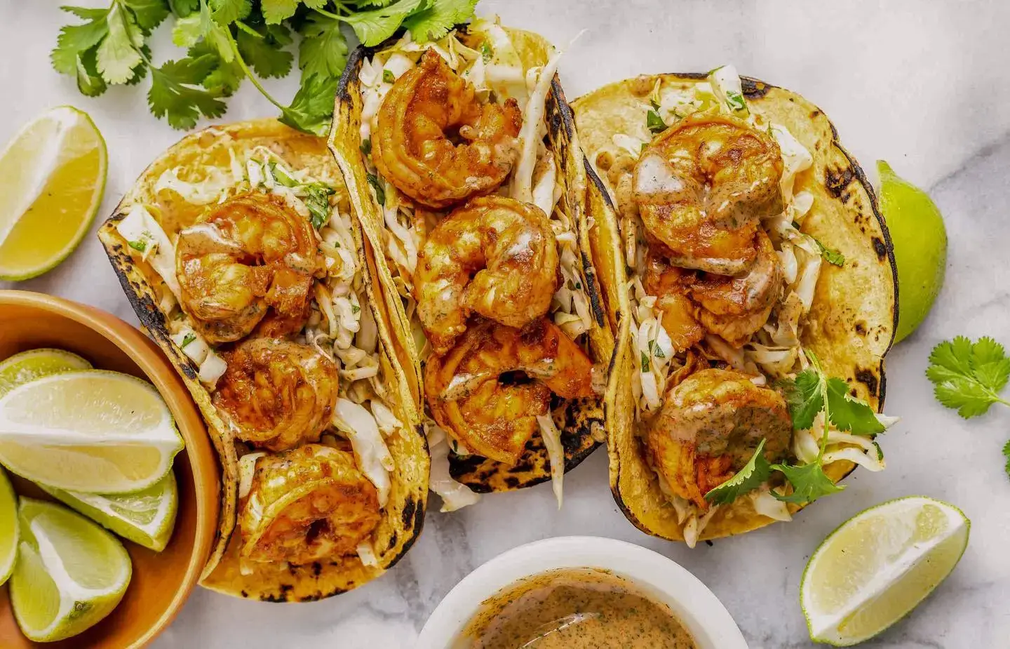 Shrimp tacos, cilantro, and limes on a marble countertop