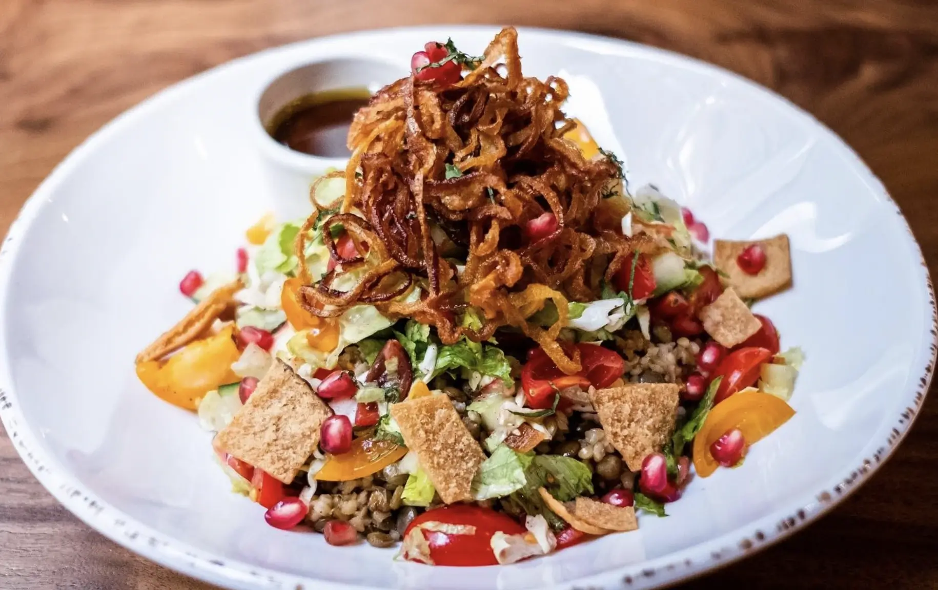 Mixed salad topped with pomegranate seeds, croutons, and fried onions with a dressing on the side of the plate