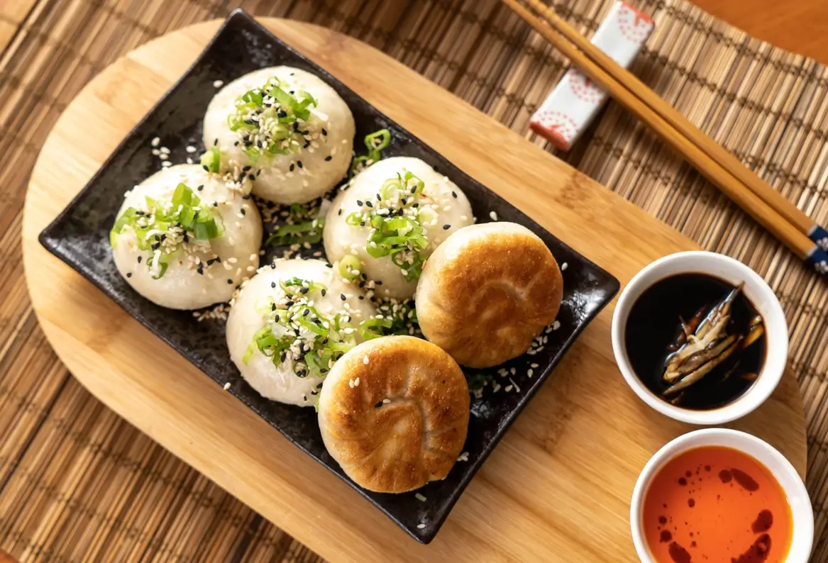 Six Chinese dumplings on a plate with dipping sauces and chopsticks