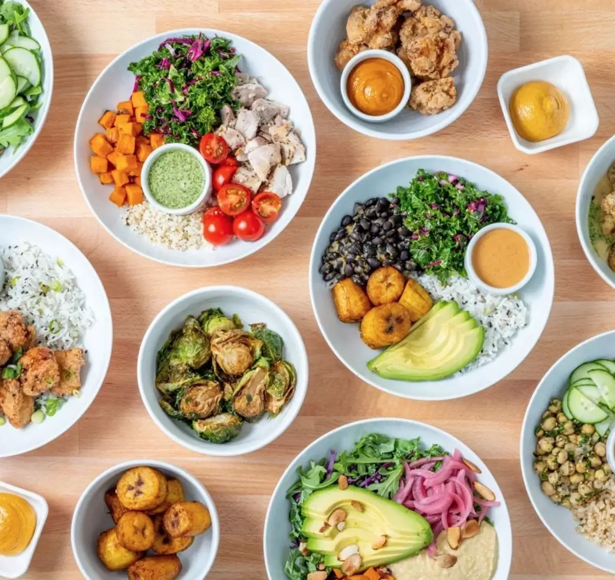 An array of healthy bowls of rice, veggies, protein, and sauces on a wooden background