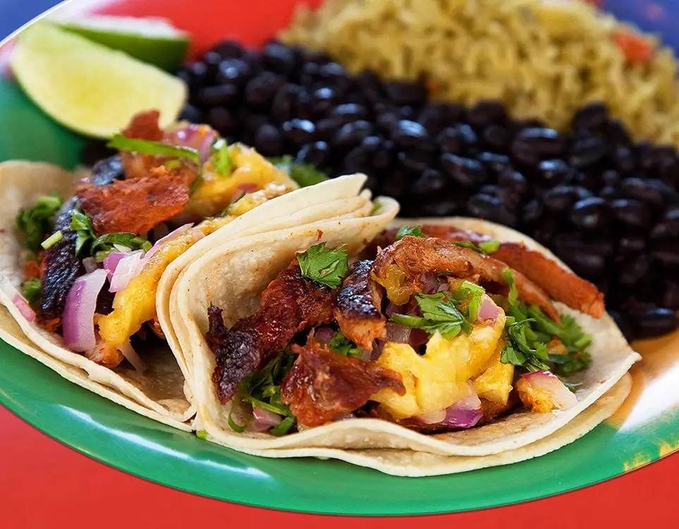 Meat and pineapple tacos, beans, rice, and limes on a green plate