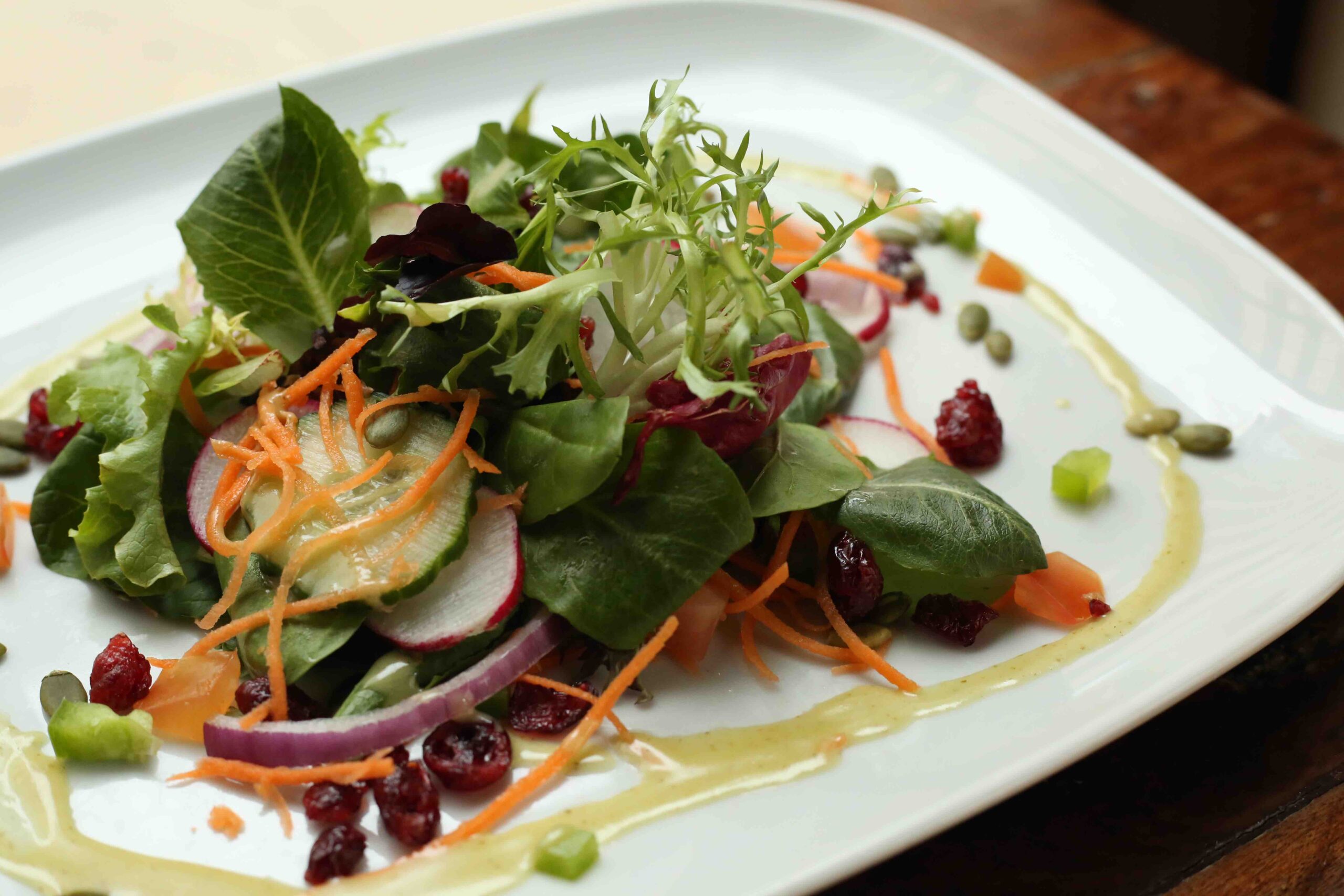 A mixed vegetable salad with a dressing drizzled along the edges of a white plate