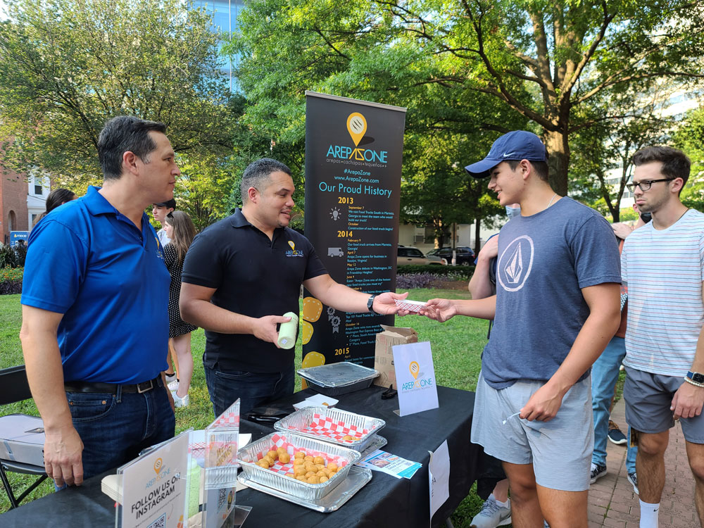 Restaurant owners providing samples to customers in an outside food market.