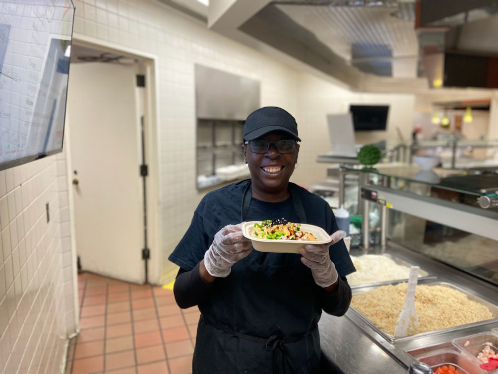 A server holding up a plate of prepared food and smiling.
