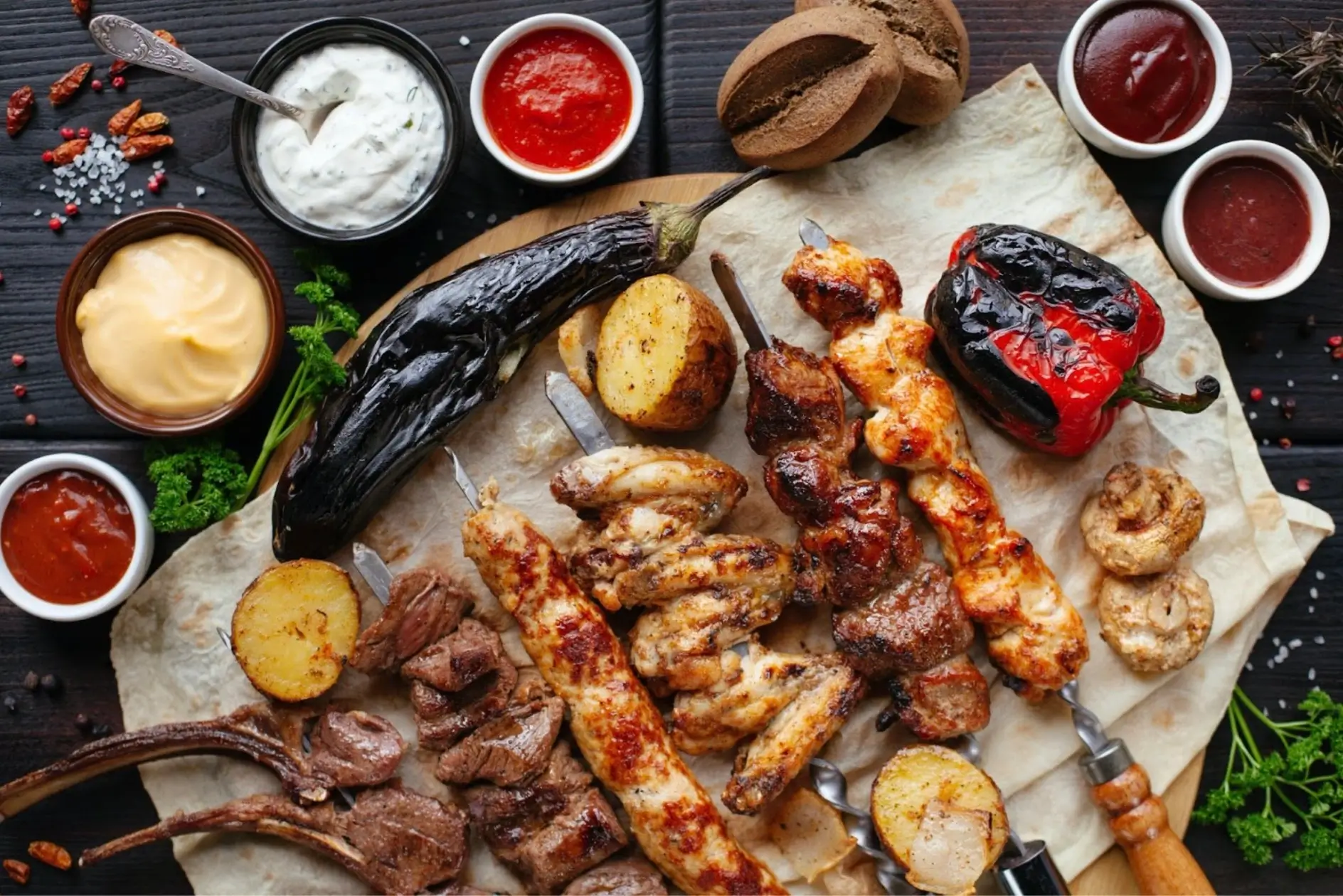 Barbequed meats, eggplant, and red pepper on a platter surrounded by small bowls of dipping sauces.