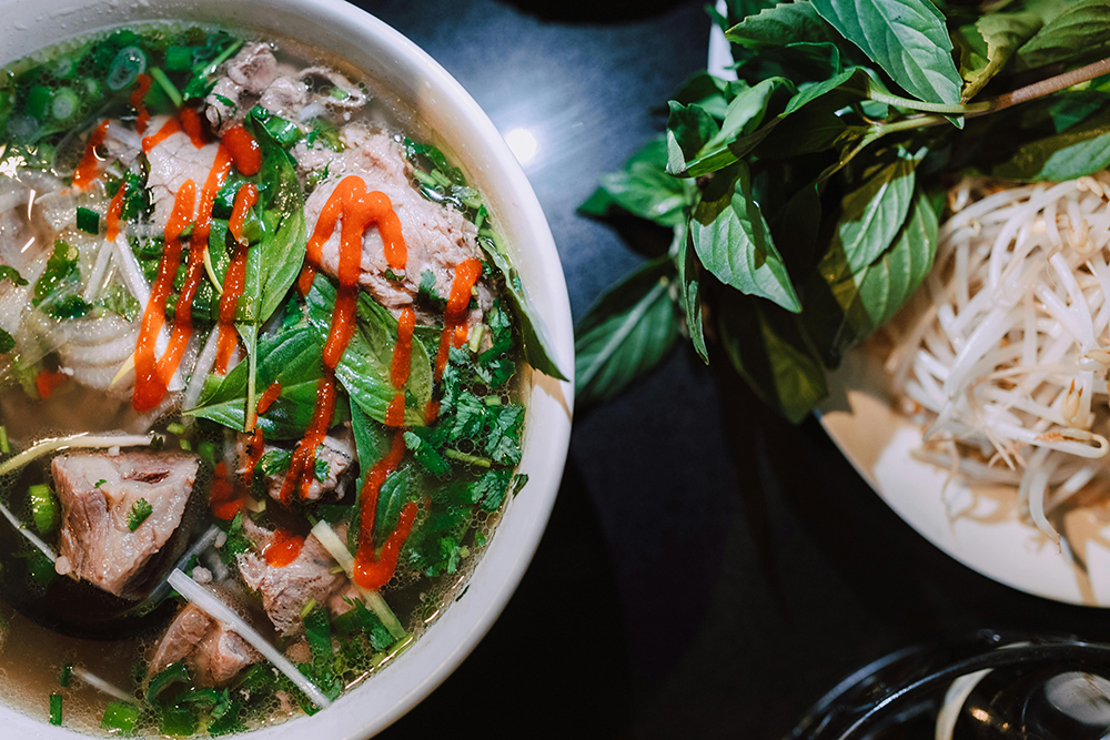 A bowl of spicy Vietnamese pho soup with basil and sprouts on the side