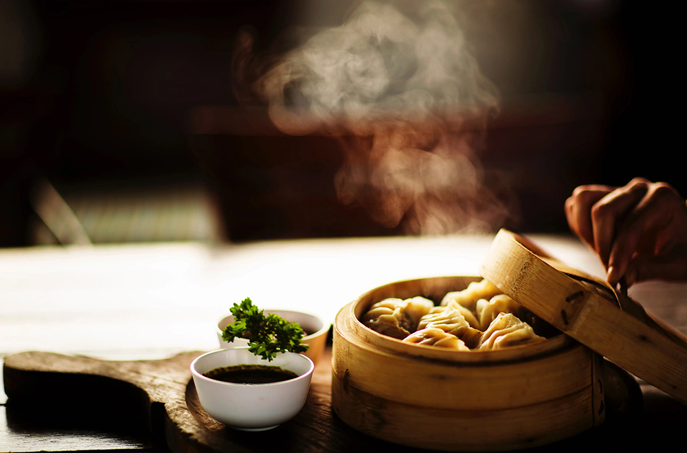 Hot dumplings in an open steamer basket with a dipping sauce and sprig of parsley