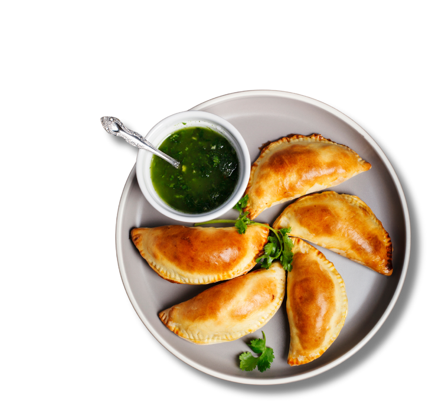 A plate of empanadas and chimichurri sauce.